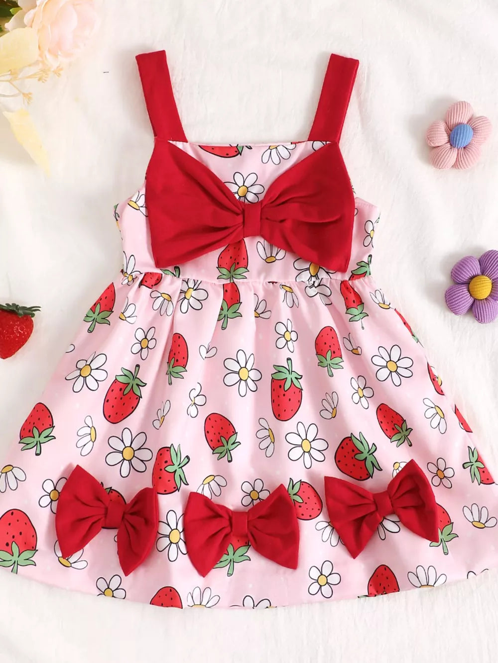 Baby dress in pink with strawberry and daisy print, featuring red bows and straps.