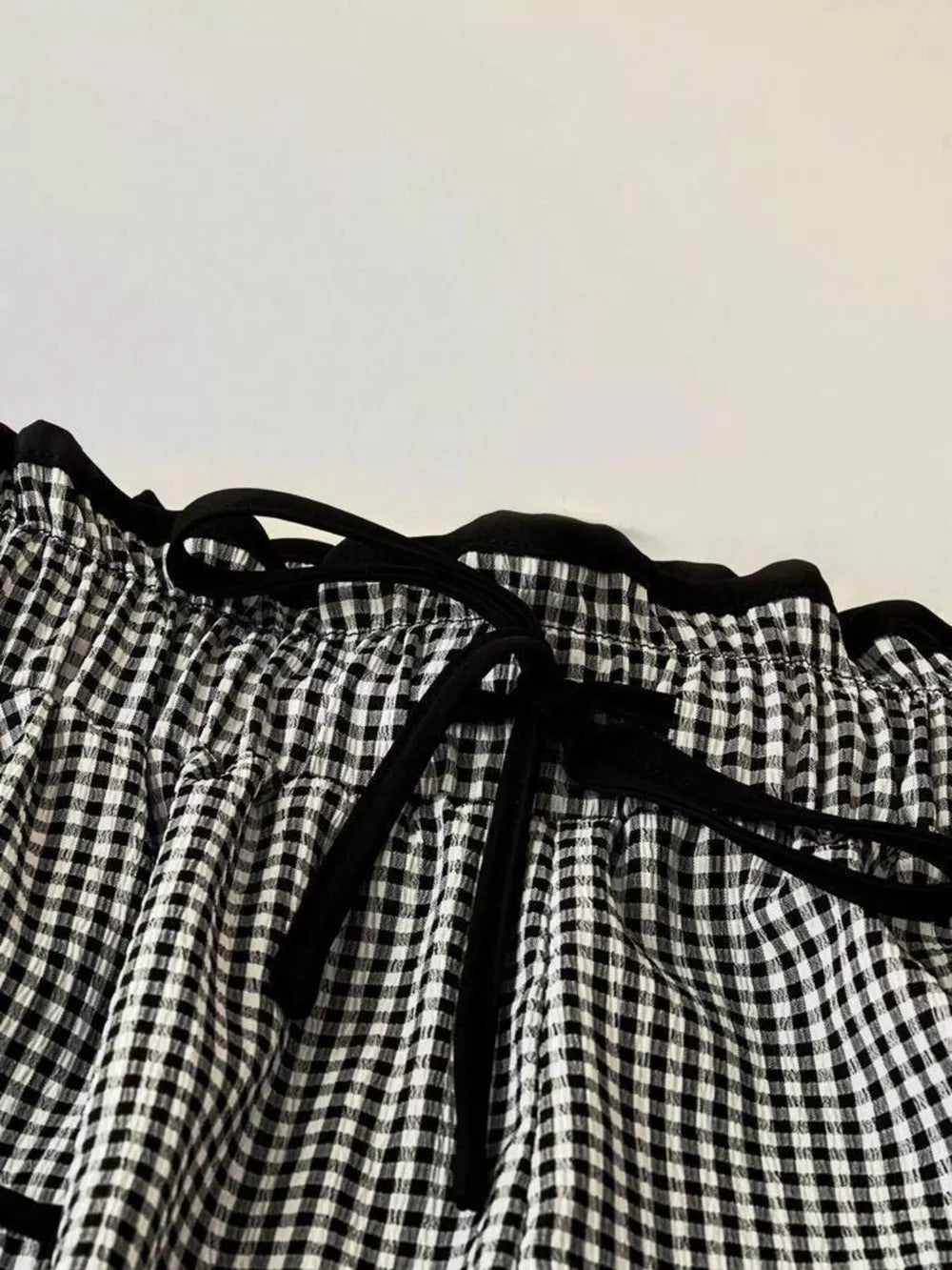 High-waisted wide-leg gingham pants with black tie detail and ruffled waist.