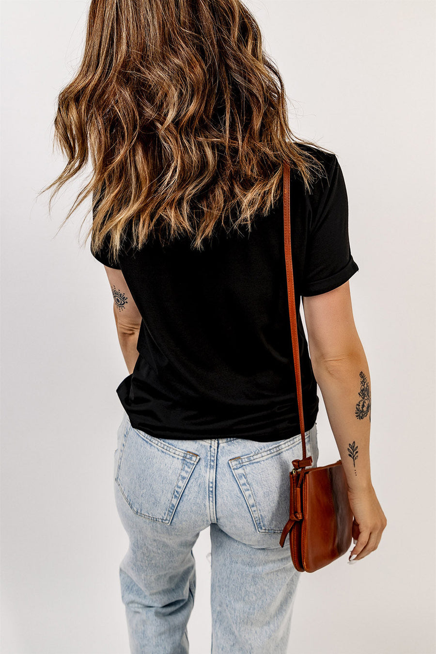 Black t-shirt with rolled sleeves and a crew neck, styled with light wash jeans and a brown crossbody bag.