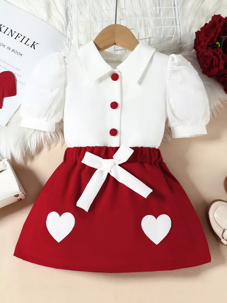 Red baby skirt with white heart appliques and white puff sleeve top with red buttons.