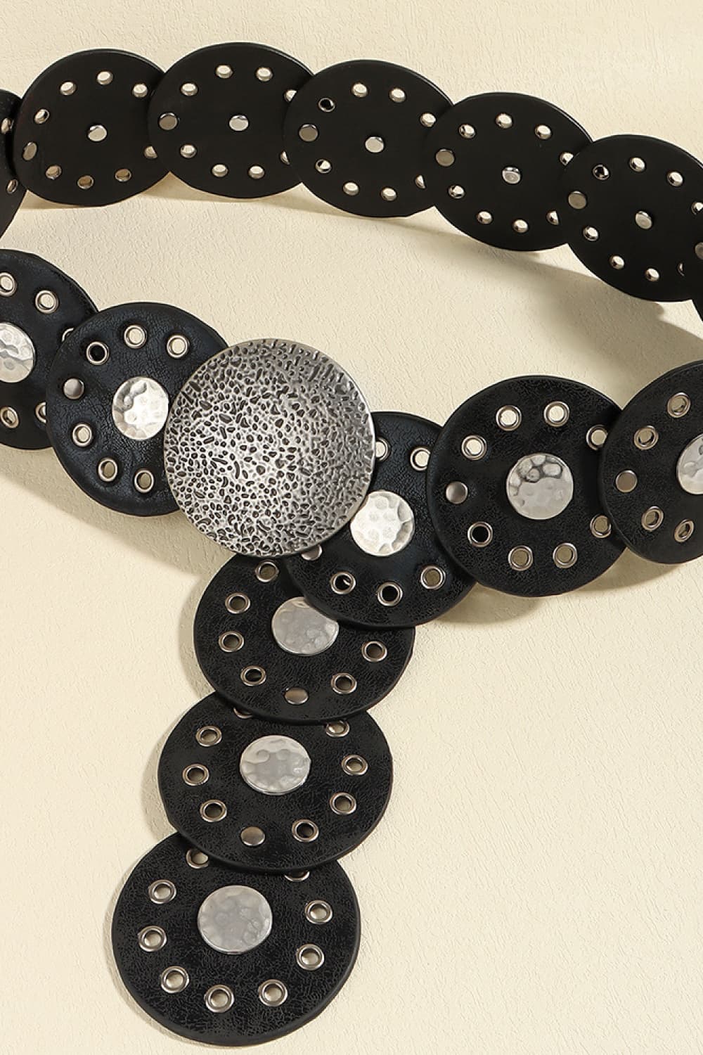 Black faux leather belt with circular discs, eyelets, and hammered silver-tone embellishments.