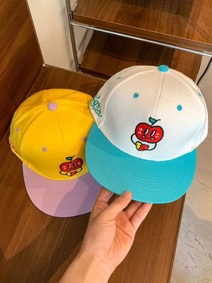 Baseball caps in yellow and white with turquoise brim, featuring embroidered apple designs.