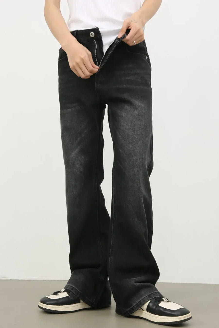Dark wash denim trousers with exaggerated flare, styled with a white tank top and sneakers.