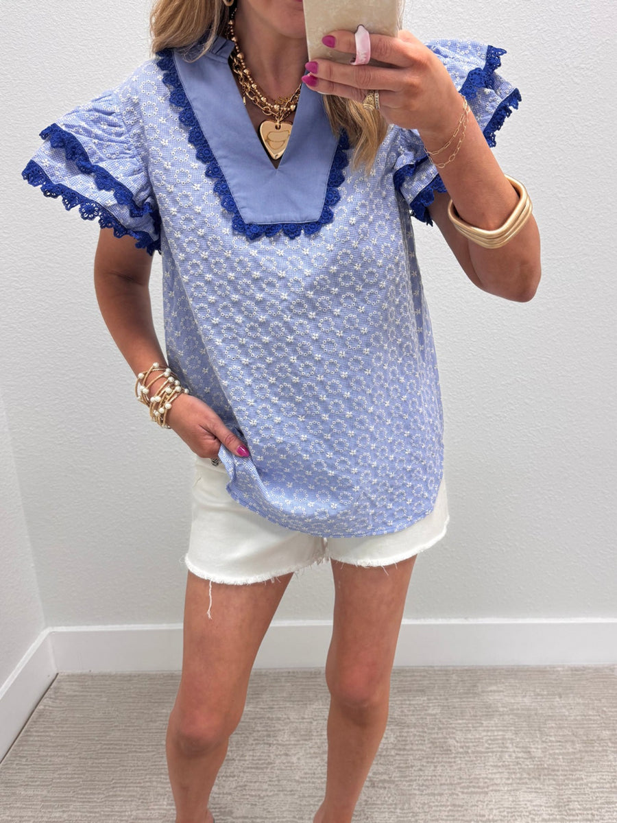 Light blue eyelet embroidered flutter sleeve blouse with lace trim and a v-neck.