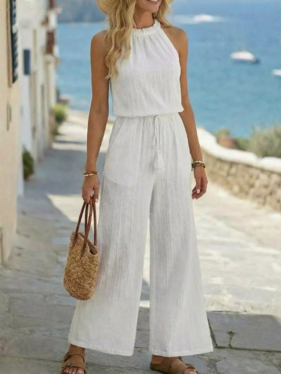 White crinkled wide-leg jumpsuit with halter neck and tassel drawstring detail.