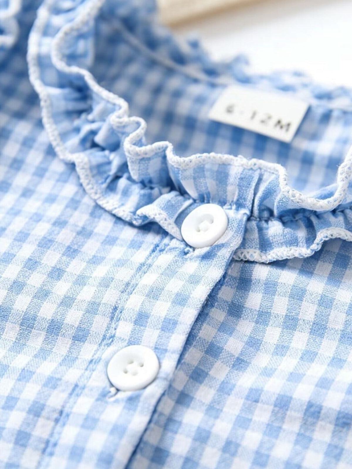 Baby dress in pastel blue gingham with white ruffled neckline and button front.