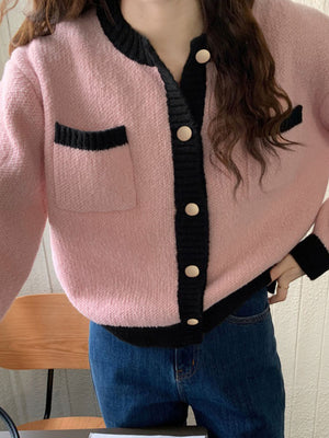 Pink acrylic cardigan with black contrast trim, buttons, and pocket detail.
