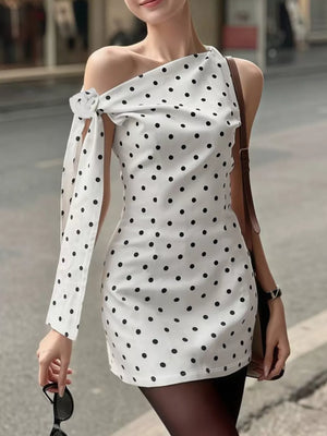 White polka dot mini dress with asymmetrical neckline and bow detail on sleeve.