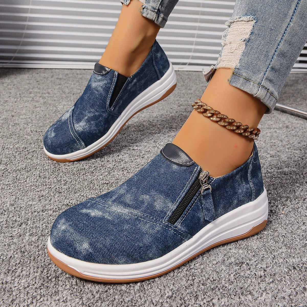Blue denim slip-on sneakers with side zipper and chunky white sole.