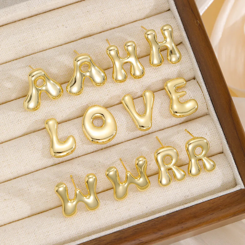 Alphabetical sculpted stud earrings in gold copper, featuring bubble letter designs.