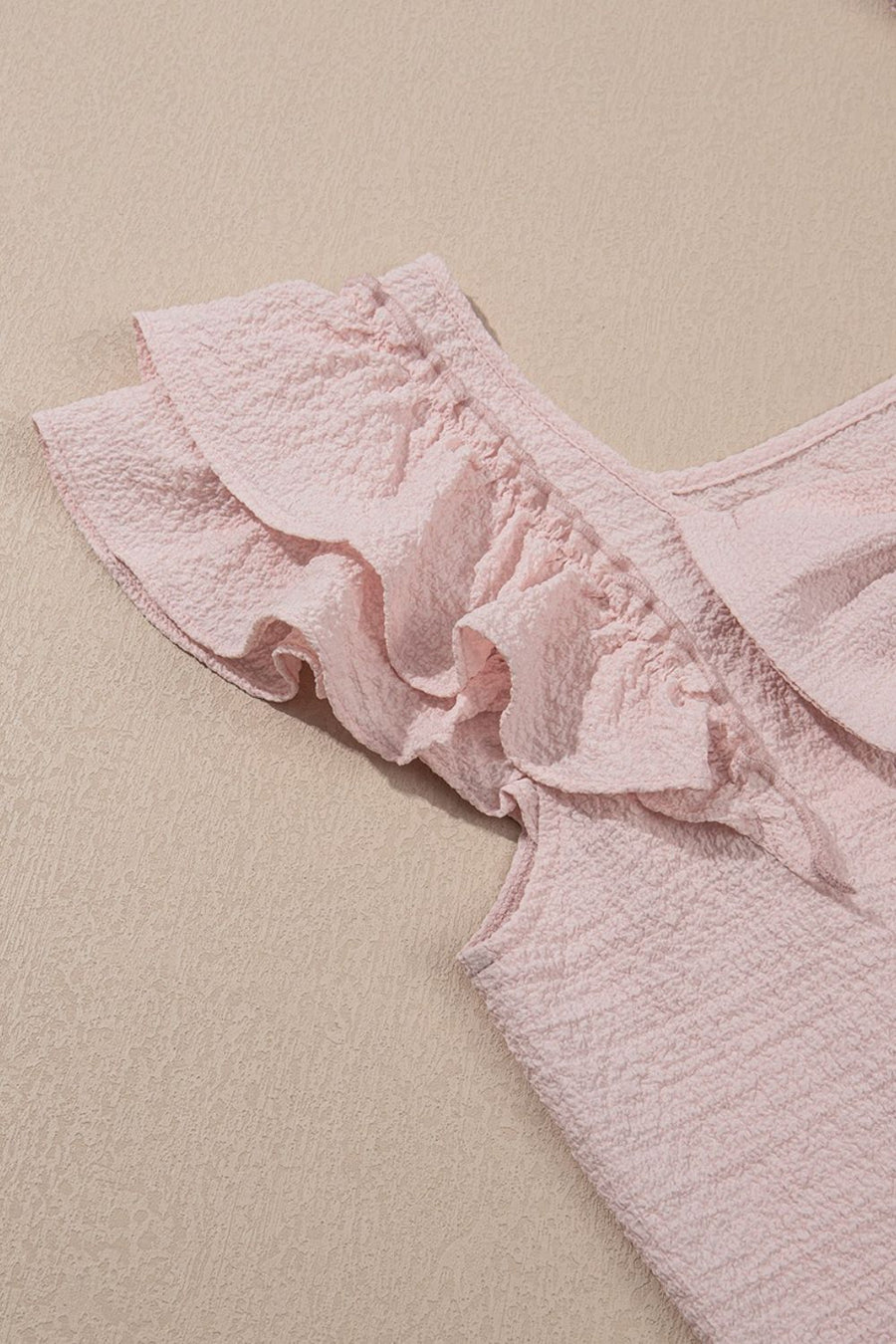 Blush pink textured blouse with ruffle cap sleeves and a V-neckline.