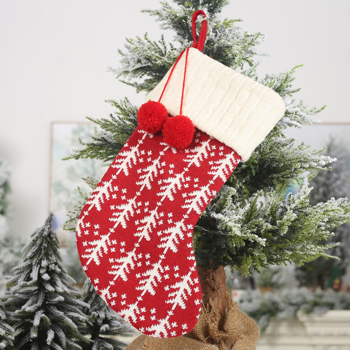 Red cable knit Christmas stocking with white tree pattern and cream cuff, two red pom-poms.