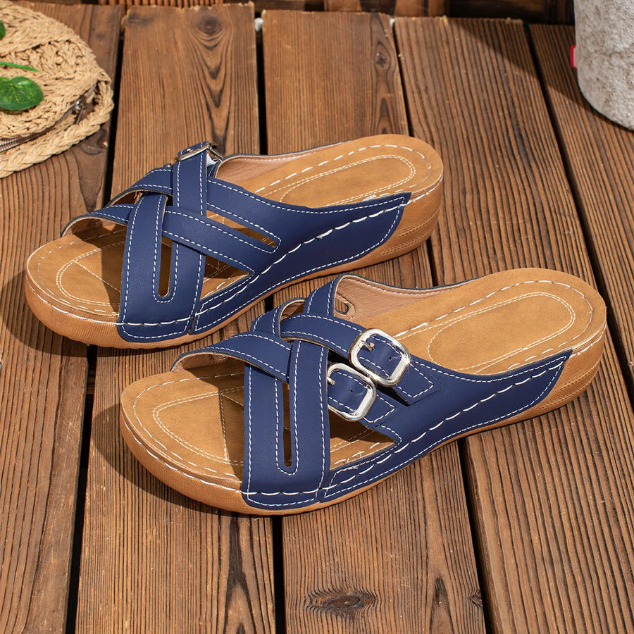 Navy crisscross buckle detail slides with white stitching on a wooden surface.