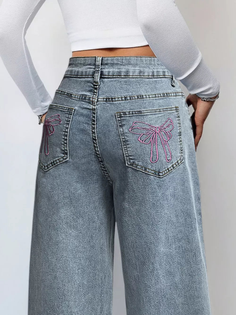 Light wash denim wide-leg jeans with pink embroidered bows on back pockets.