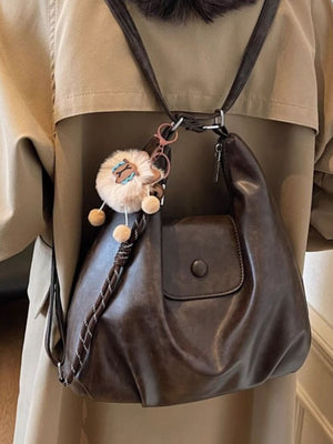Slouchy coffee brown pu leather shoulder bag with braided strap detail and fluffy charm.