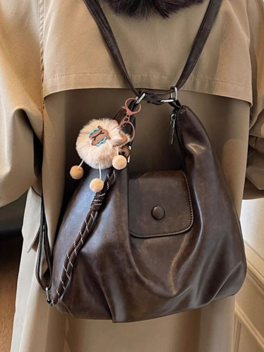 Slouchy coffee brown pu leather shoulder bag with braided strap detail and fluffy charm.