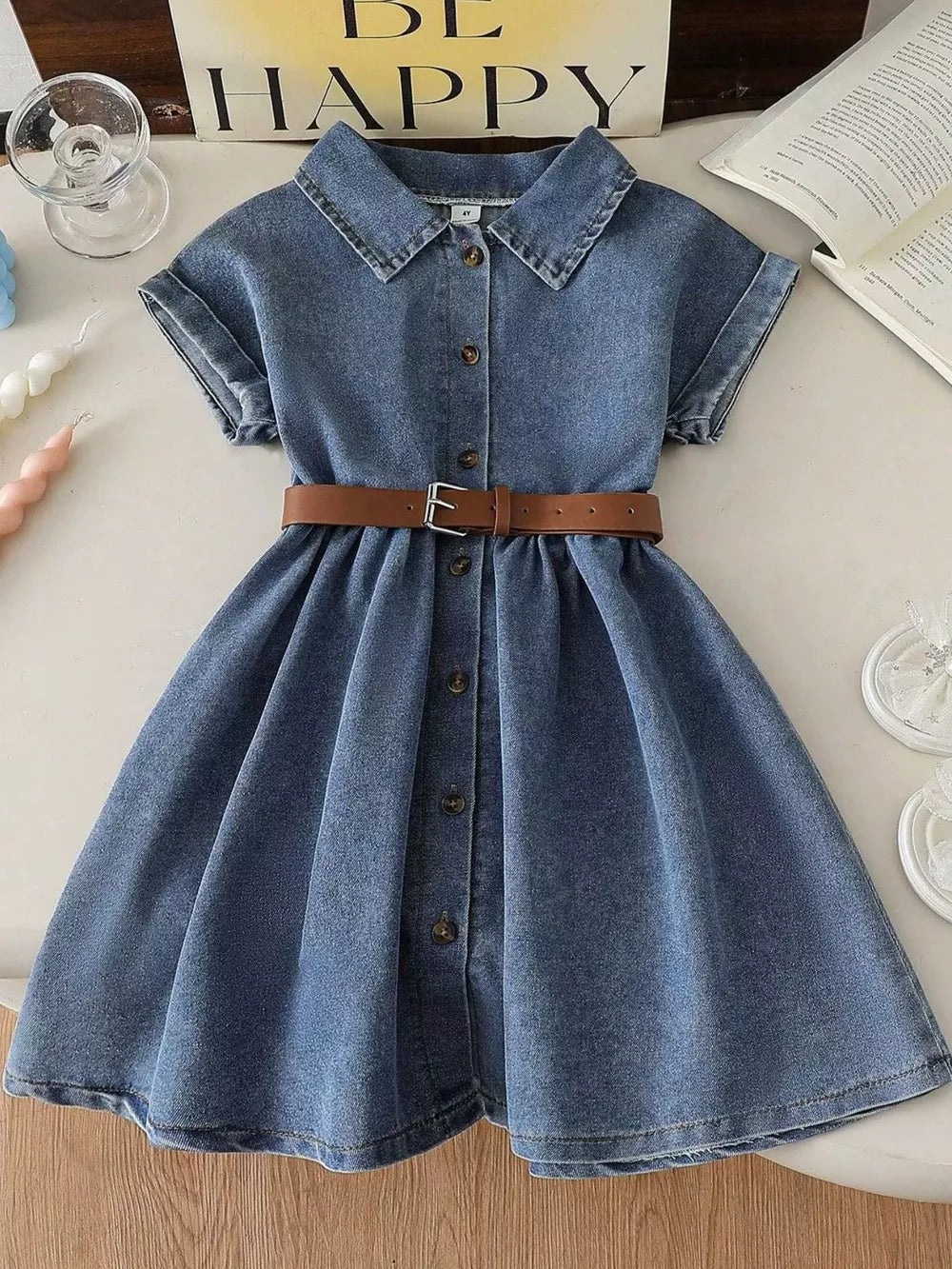Blue denim baby dress with short sleeves, button front, collar, and brown belt.