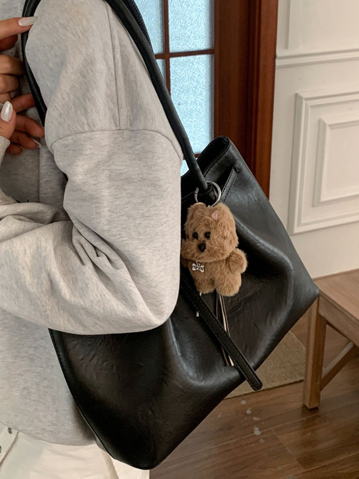 Black leather shoulder bag with buckle detail and a fluffy dog charm.