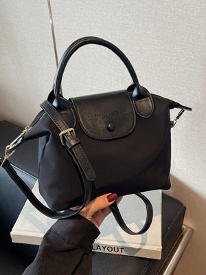 Black nylon crossbody bag with leather flap and top handle, adjustable strap.