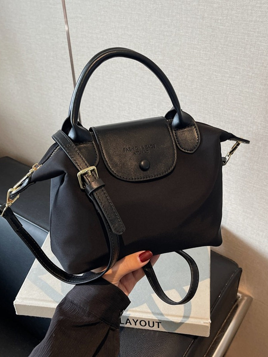 Black nylon crossbody bag with leather flap and top handle, adjustable strap.