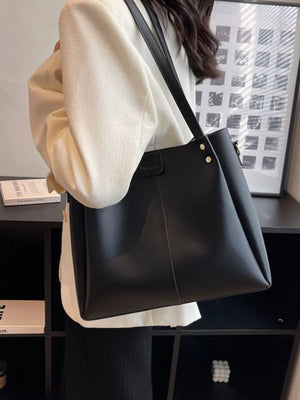 Black PU leather trapezoid bag with wide straps and gold hardware detail.
