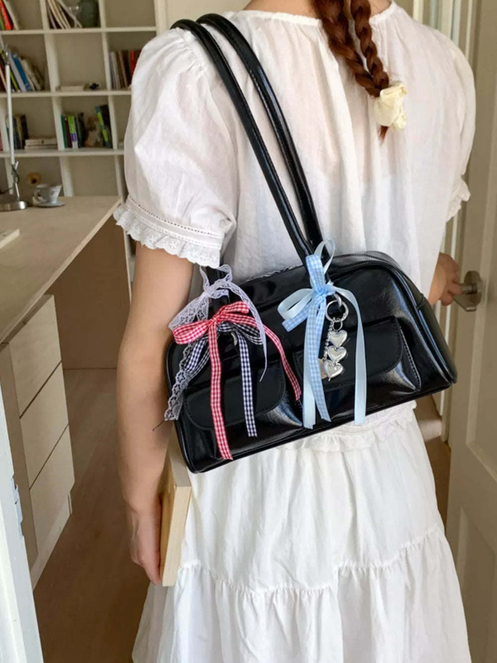Black shoulder bag with ribbon and heart charms, styled with a white dress.
