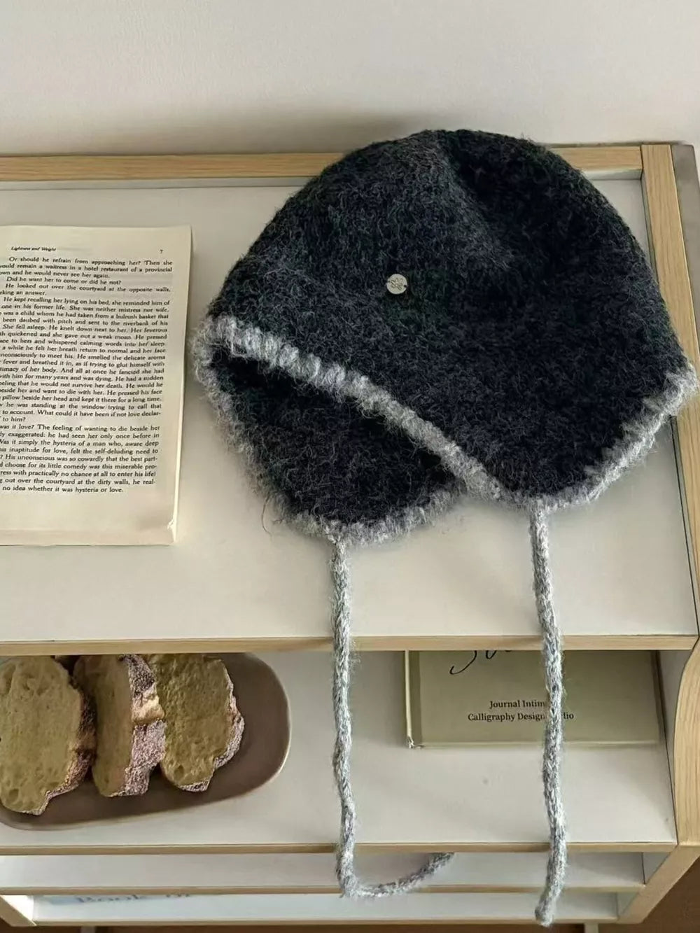 Gray wool-blend hat with ear flaps and braided ties, contrast trim.