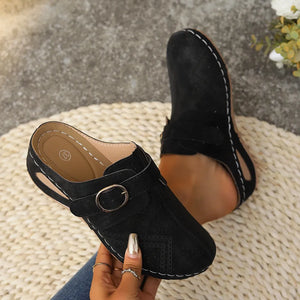 Black laser-cut buckle mule wedges with white stitching and a gold buckle detail.