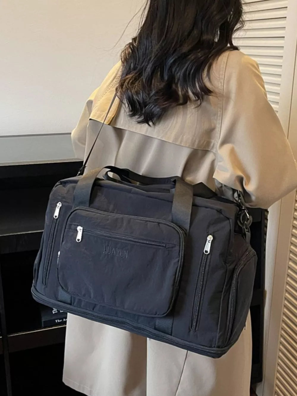 Black canvas duffel bag with multiple zippered pockets and embroidered text.