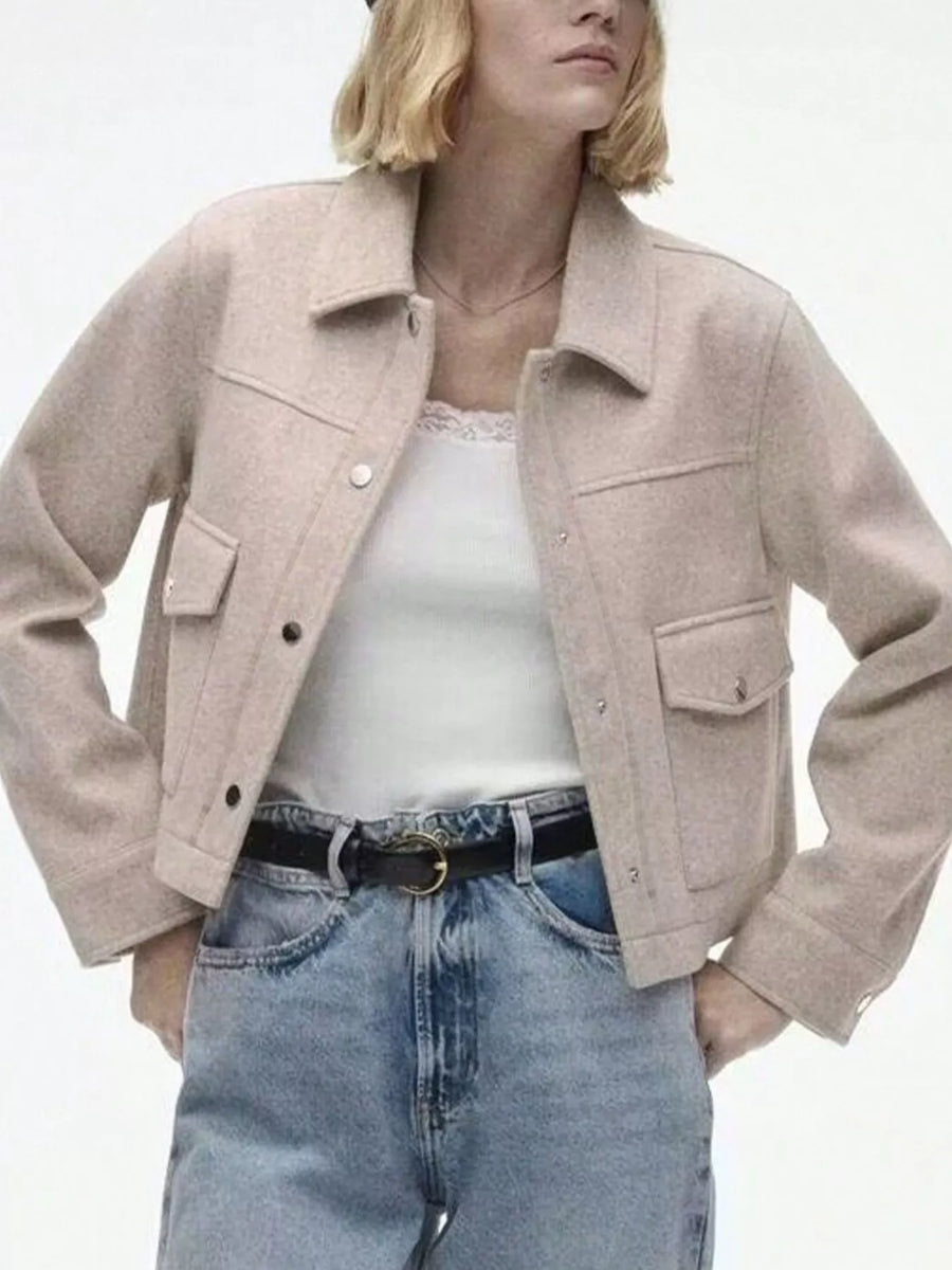 Beige trucker jacket with snap buttons, chest pockets, and collar, styled with a white cami and jeans.