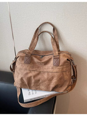 Brown suede duffel bag with top handles and adjustable strap, front zip pocket.