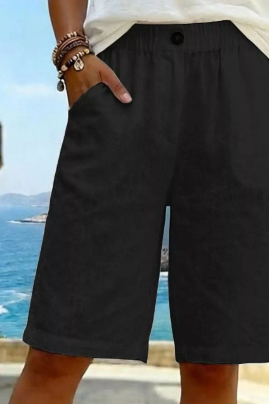 Black knee-length shorts with pockets and a button closure, styled with bracelets.