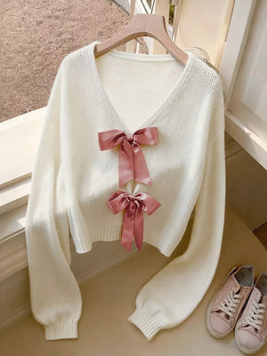 White acrylic knit V-neck cardigan with two pink bow embellishments and balloon sleeves.