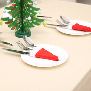 Red Santa hat cutlery holders with white trim and pom-poms on white plates.