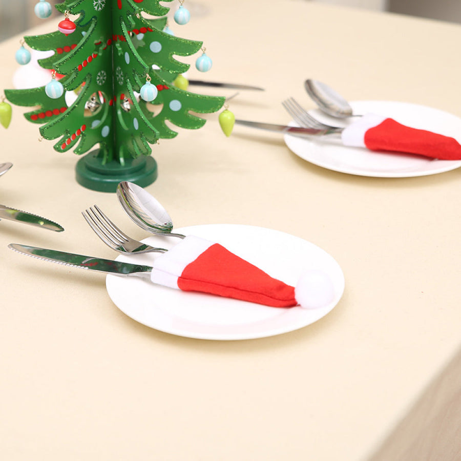 Red Santa hat cutlery holders with white trim and pom-poms on white plates.