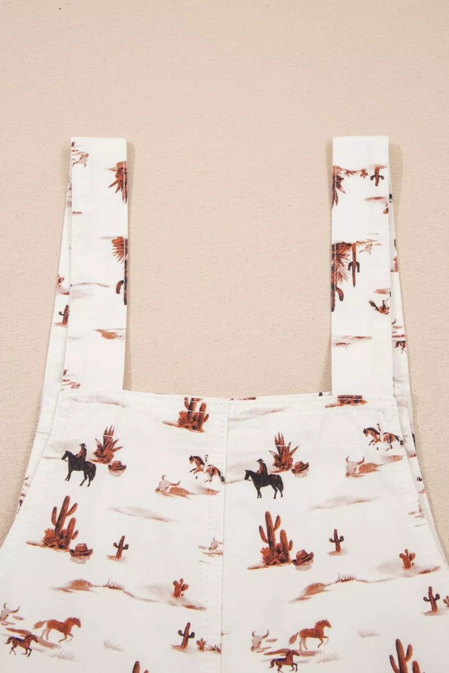 White cotton jumpsuit with desert motif, cowboys, horses, and cacti pattern.