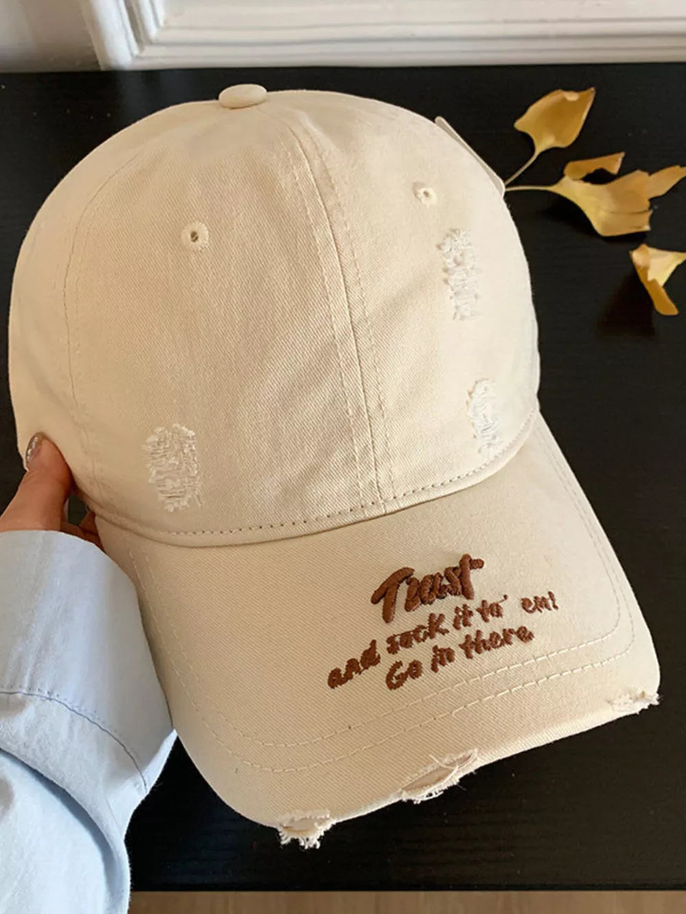 Beige distressed baseball hat with embroidered text and frayed details.