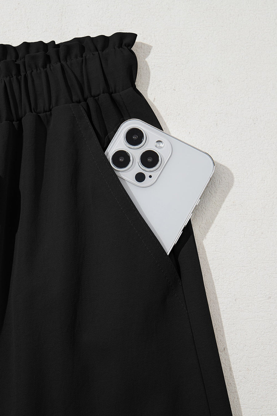Black cropped drawstring pants with elastic waist and pocket holding a smartphone.