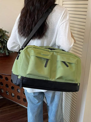 Green duffle bag with black accents and front pockets, worn over the shoulder.