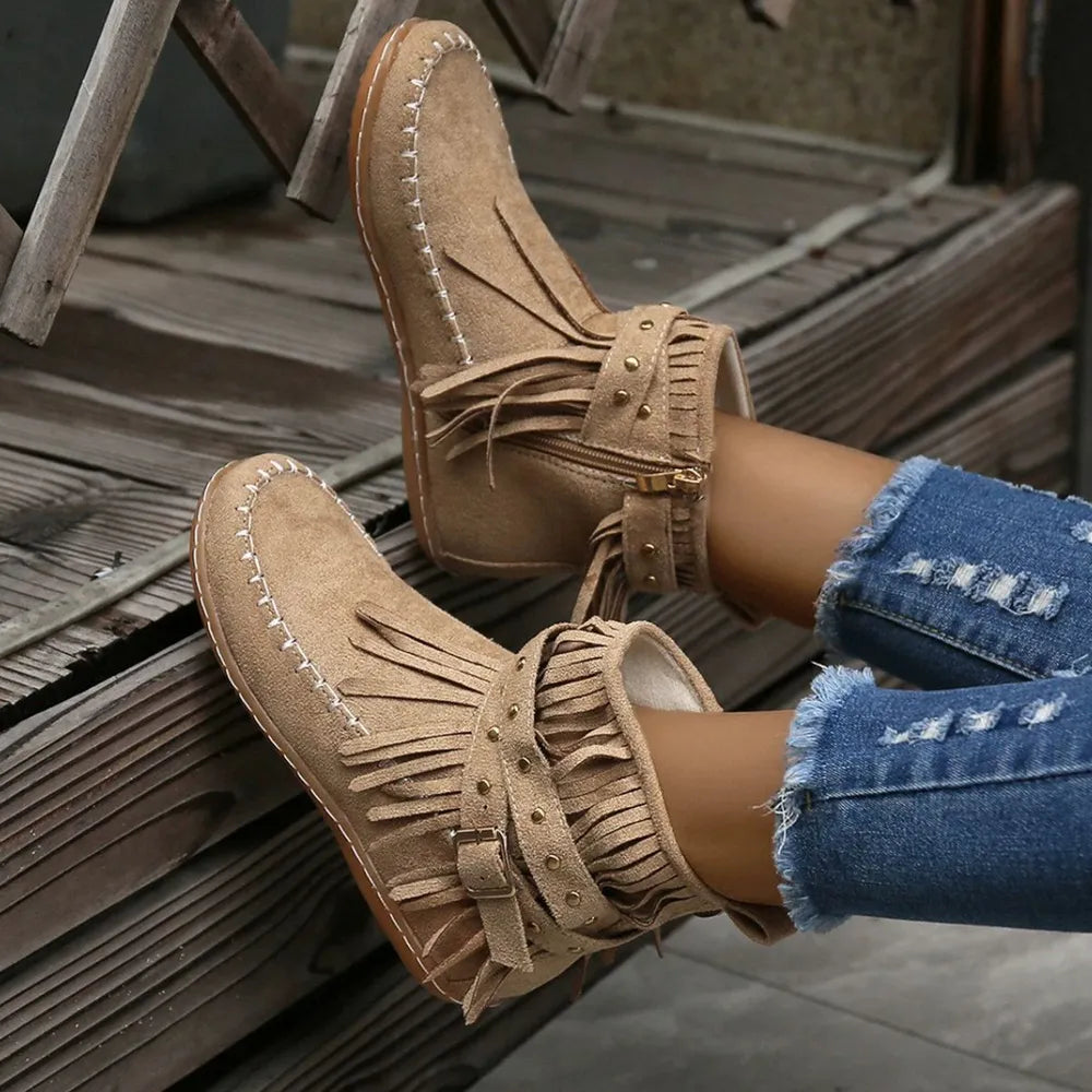 Beige suede ankle boots with fringe, studs, and buckle detail.