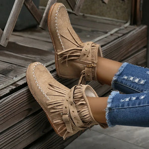 Beige suede ankle boots with fringe, studs, and buckle detail.