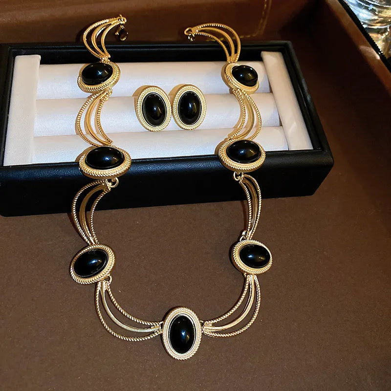 Gold oval gemstone necklace and matching earrings set with black stones.