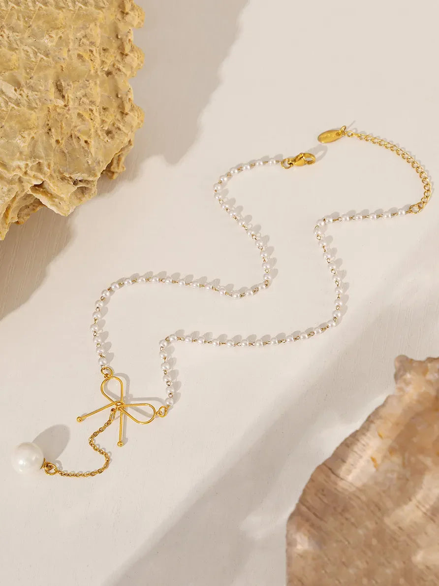 Gold lariat necklace with pearl beads, a bow detail, and a single pearl drop.