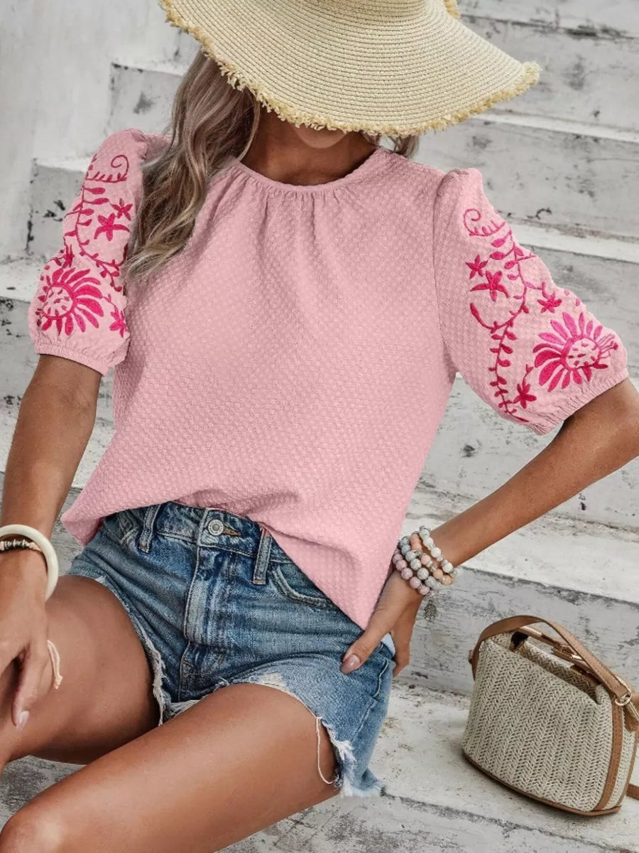 Pink embroidered puff sleeve blouse with textured fabric and round neckline.