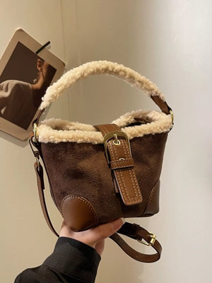 Brown suede bucket bag with fuzzy trim and buckle detail, crossbody strap.
