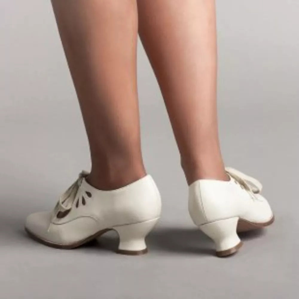 White leather lace-up heels with cut-out details and a bow accent.
