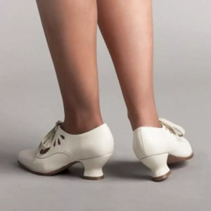 White leather lace-up heels with cut-out details and a bow accent.
