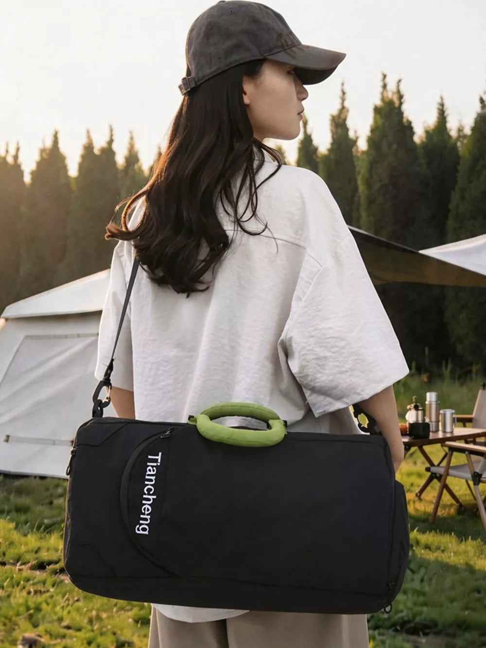 Black duffel bag with green handles and white text, worn by a person with a baseball cap.