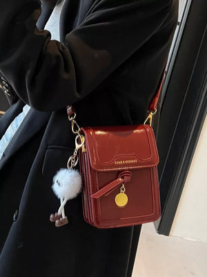 Deep Red mini crossbody bag in patent pu leather with gold charm and fluffy keychain.