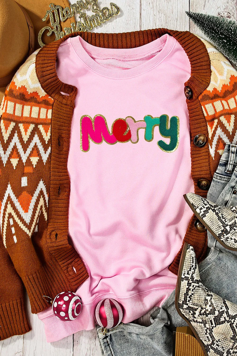Blush pink crewneck sweatshirt with embroidered colorful "Merry" text and gold trim.